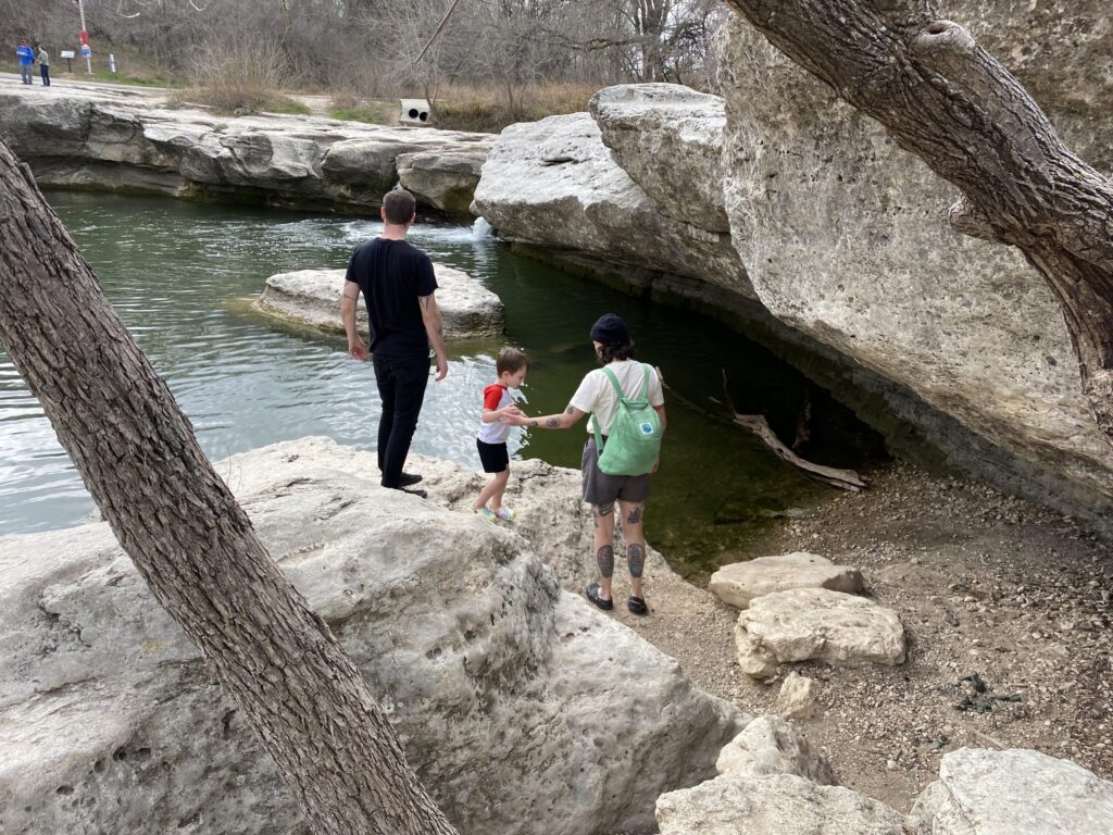 Family of three walking on rocks at McKinney Falls State Park, which you can reach easily with a group rental van