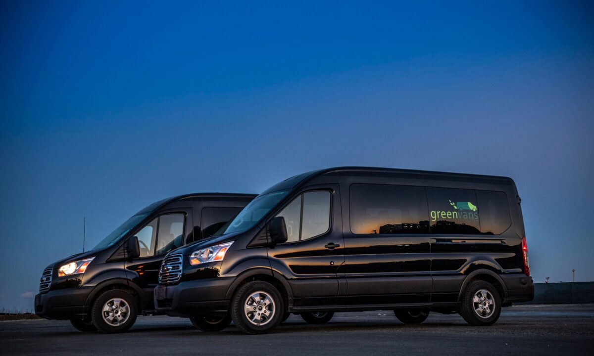 Side view of two Greenvans Ford 15 passenger transit vans parked at night