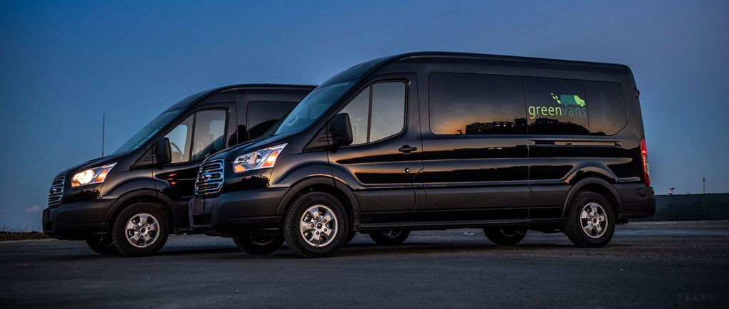 Side view of two Ford Transit 15-passenger rental vans with the Greenvans logo