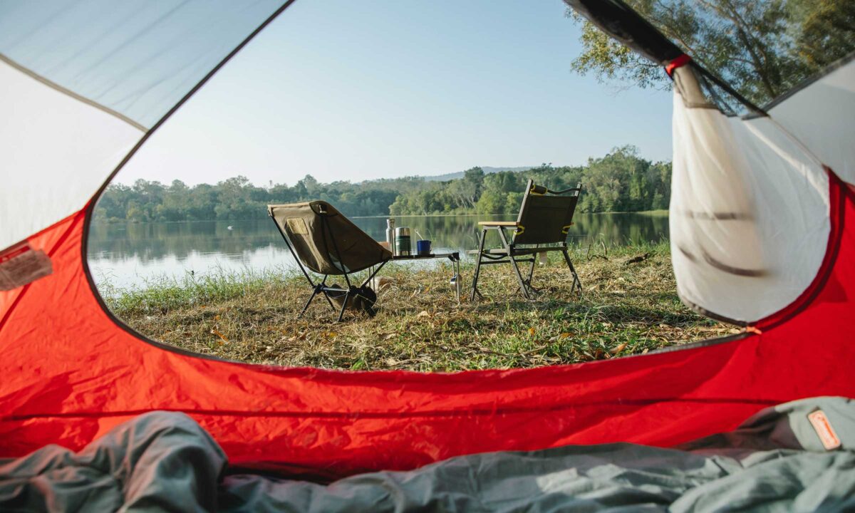 A camp site with a tent and two chairs by a lake