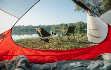 A camp site with a tent and two chairs by a lake