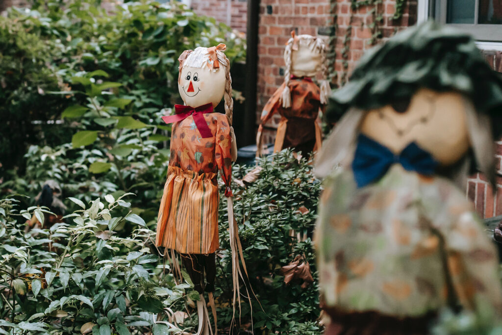 Three friendly scarecrows displayed outside red brick house
