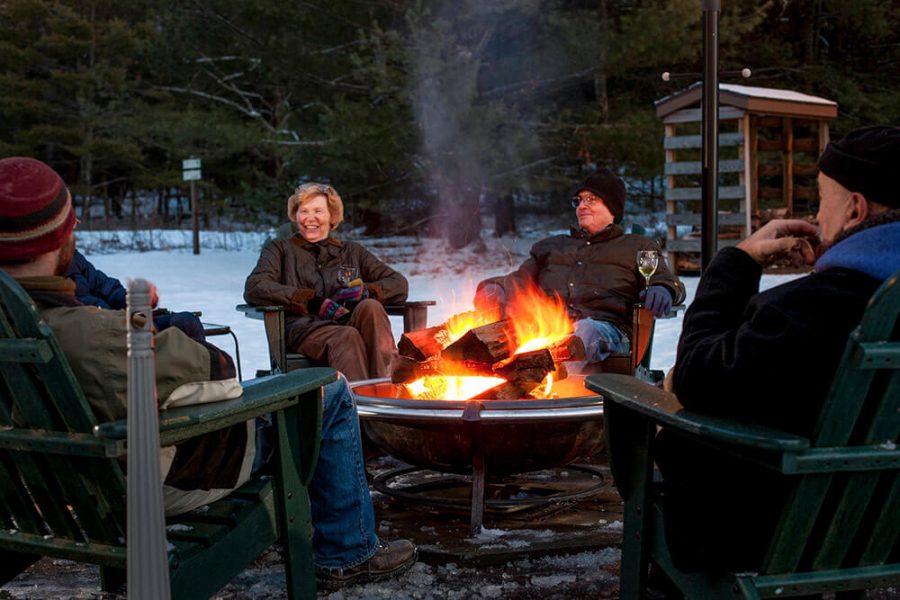 Four adults sitting around a fire pit in the winter when there is snow on the ground