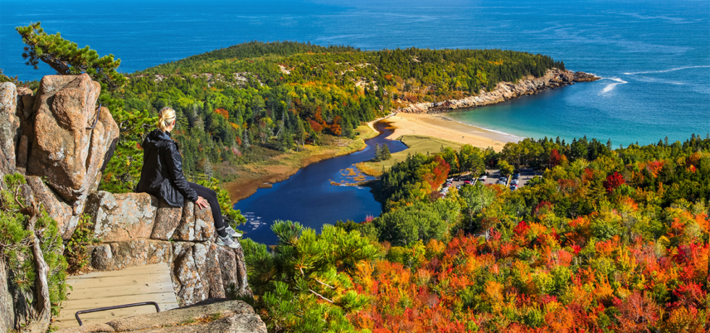 Woman sitting on boulders overlooking the water at Acadia in Bar Harbor, Maine