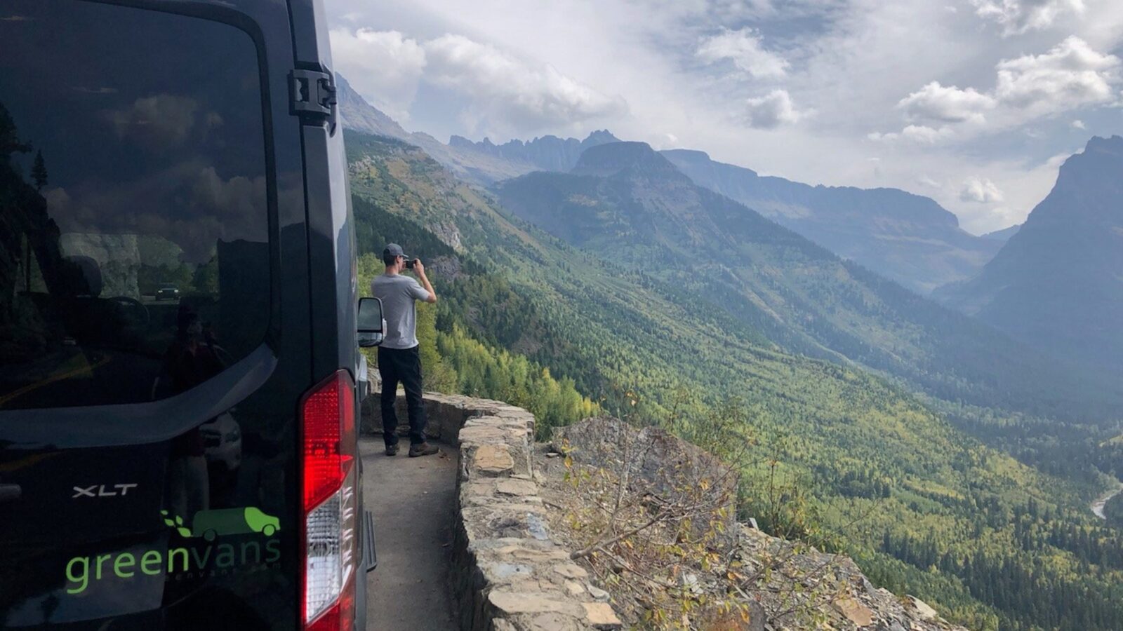 Man standing outside a Greenvans 15-passenger rental taking pictures of the mountainside