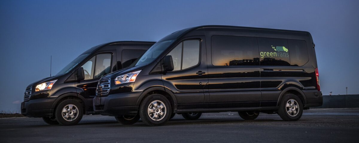 Side view of two Ford 15 Passenger Medium Roof Transit 350 XLT rental vans with Greenvans logo