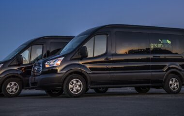 Side view of two Ford 15 Passenger Medium Roof Transit 350 XLT rental vans with Greenvans logo.