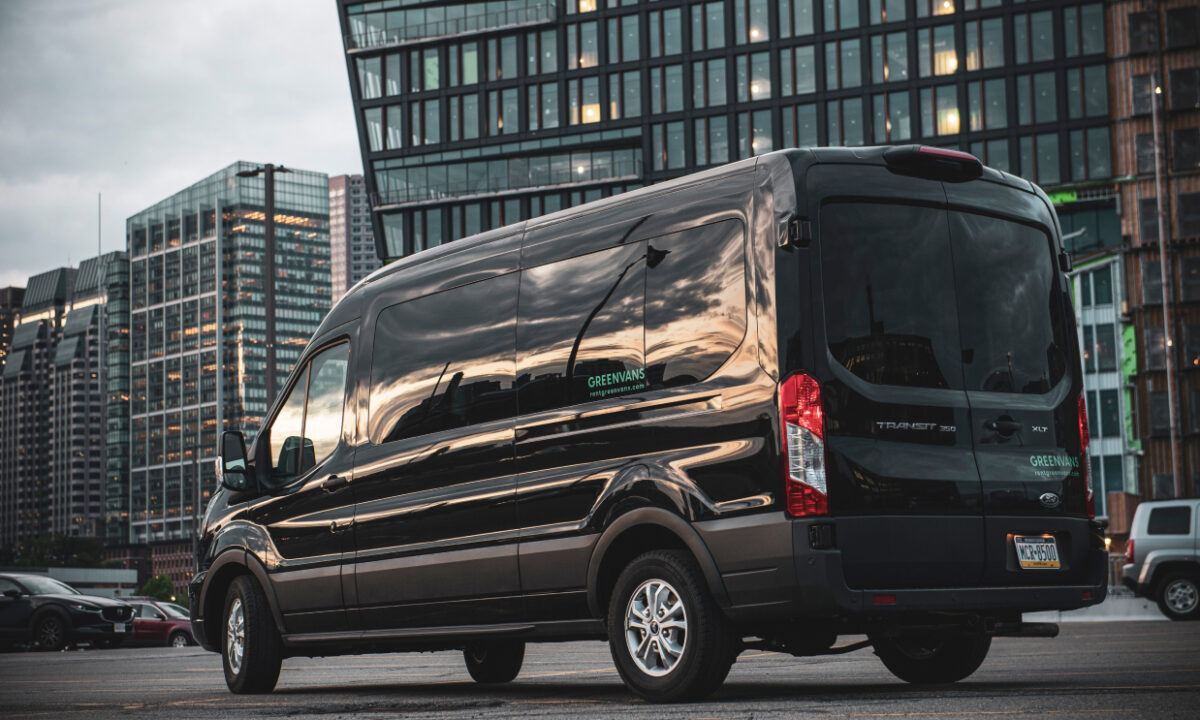 A black Ford Transit 15 passenger van in front of office buildings on a gray day