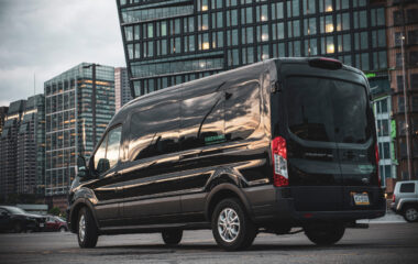 A black Ford Transit 15 passenger van in front of office buildings on a gray day